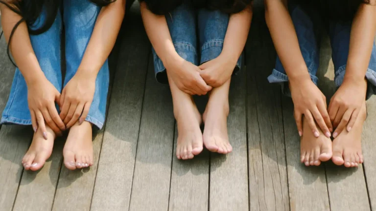 3 women in jeans sitting barefoot on sun-bleached wooden planks