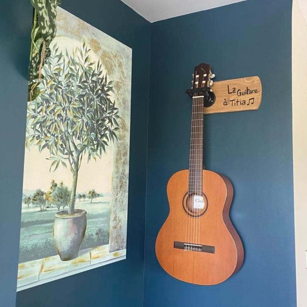 support-guitare-mural-cadeau-bois-personnalisé-artisanal Guitare classique accrochée au mur bleu.