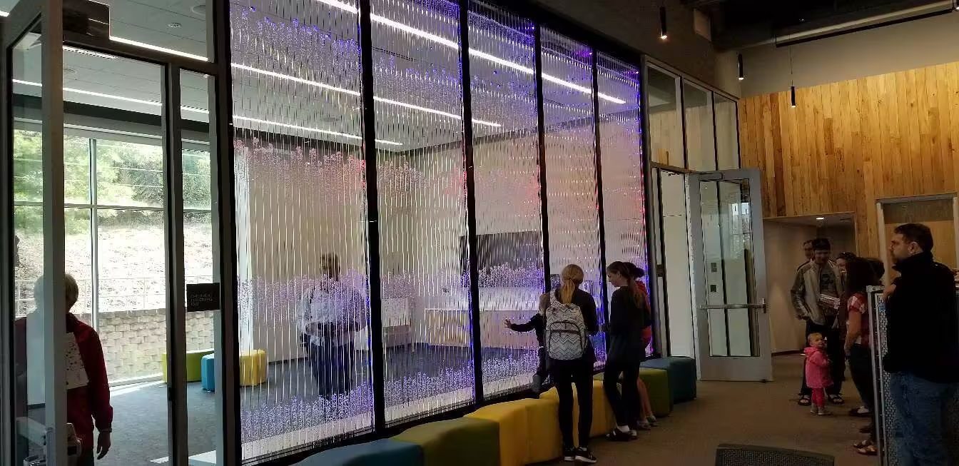 Interior waterfall wall installation with colorful LED lighting, featuring people interacting and admiring the design in a modern commercial space.