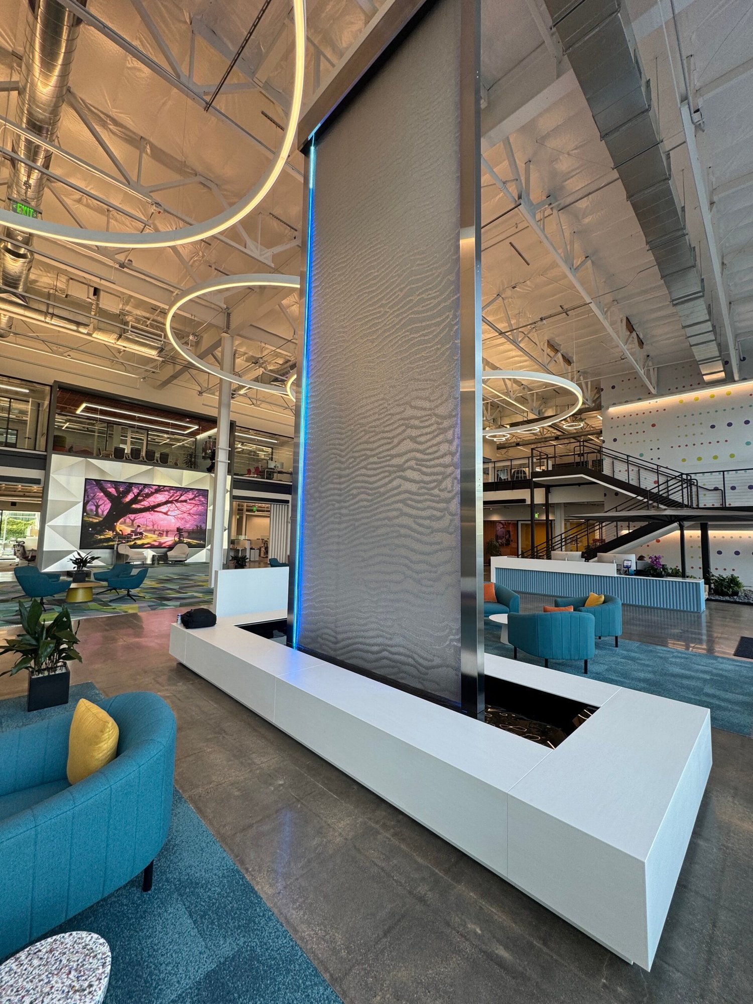 Floor Fountain 2 Indoor floor water fountain with illuminated water feature, modern design, surrounded by contemporary seating and vibrant decor in a spacious interior.