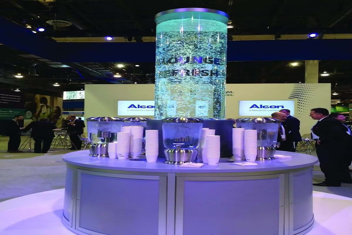 Indoor water feature with bubble wall design, showcasing a refreshing lounge area at a commercial event, surrounded by attendees and branded elements for Alcon.