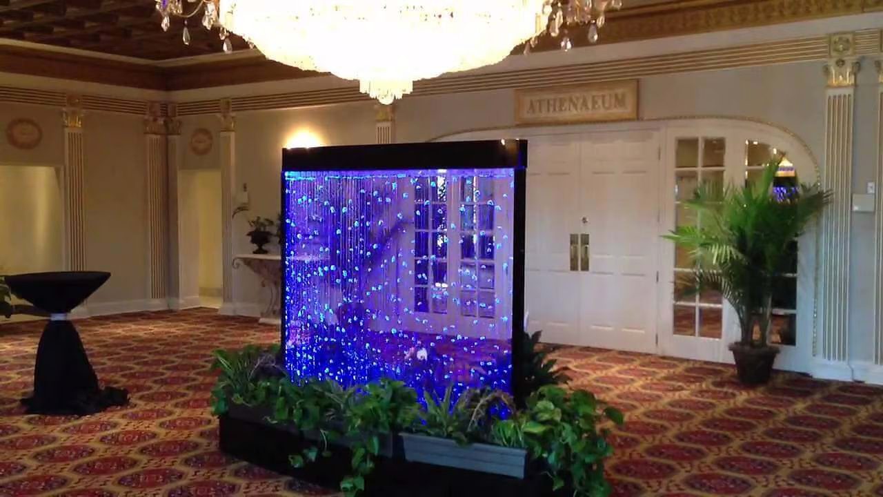 Indoor waterfall wall feature with illuminated bubbles, enhancing the ambiance of a luxurious commercial space, surrounded by lush greenery and elegant decor.