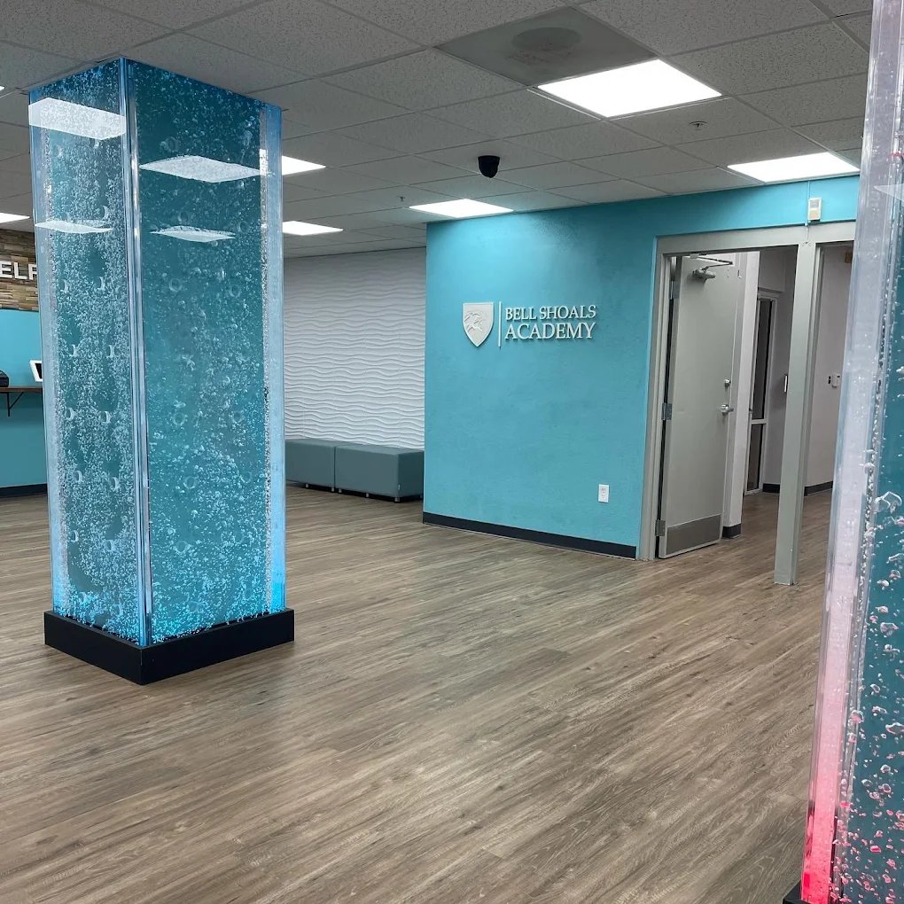 Rod-Swirley-Bubble Wall for Bell Shoals Academy in Brandon, Florida Bubble wall column at Bell Shoals Academy, enhancing the reception area with soothing movement and ambiance, featuring blue and red lighting against a modern interior design.