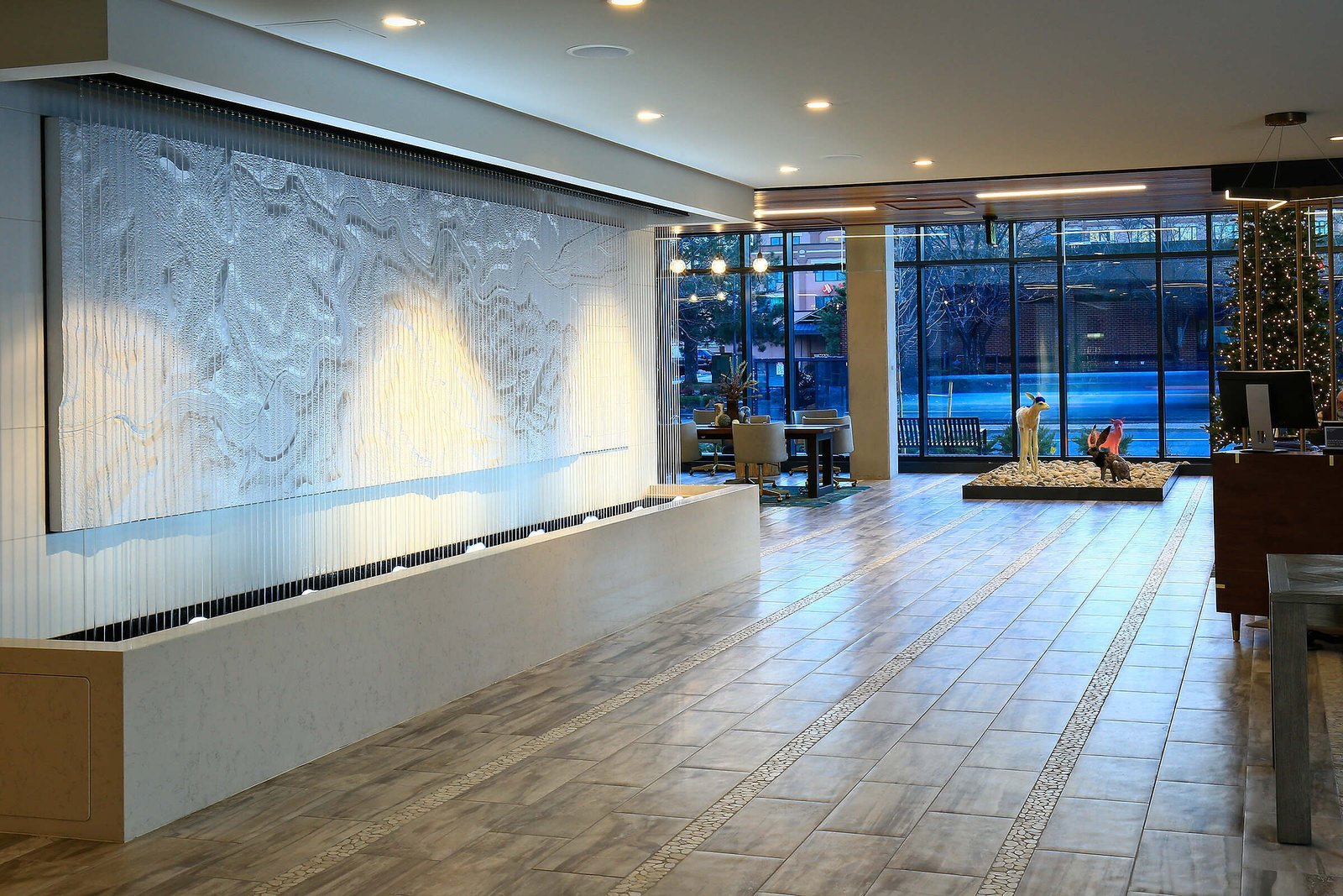 Rain Curtain with Bubbler Jets at Embassy Suites Boulder, Colorado (1) Rain curtain water feature with bubbler jets in hotel lobby, enhancing ambiance and tranquility, surrounded by modern furnishings and large windows.