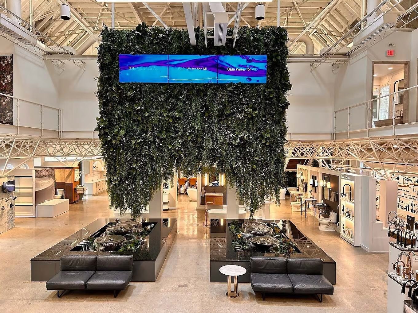 Indoor water feature with lush greenery, sleek black seating, and digital screens displaying "Safe Water for All," enhancing the modern design of a business space.