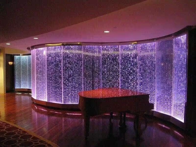 Indoor bubble wall with illuminated water features and a grand piano in a modern commercial space, showcasing aesthetic design elements for enhancing environments.