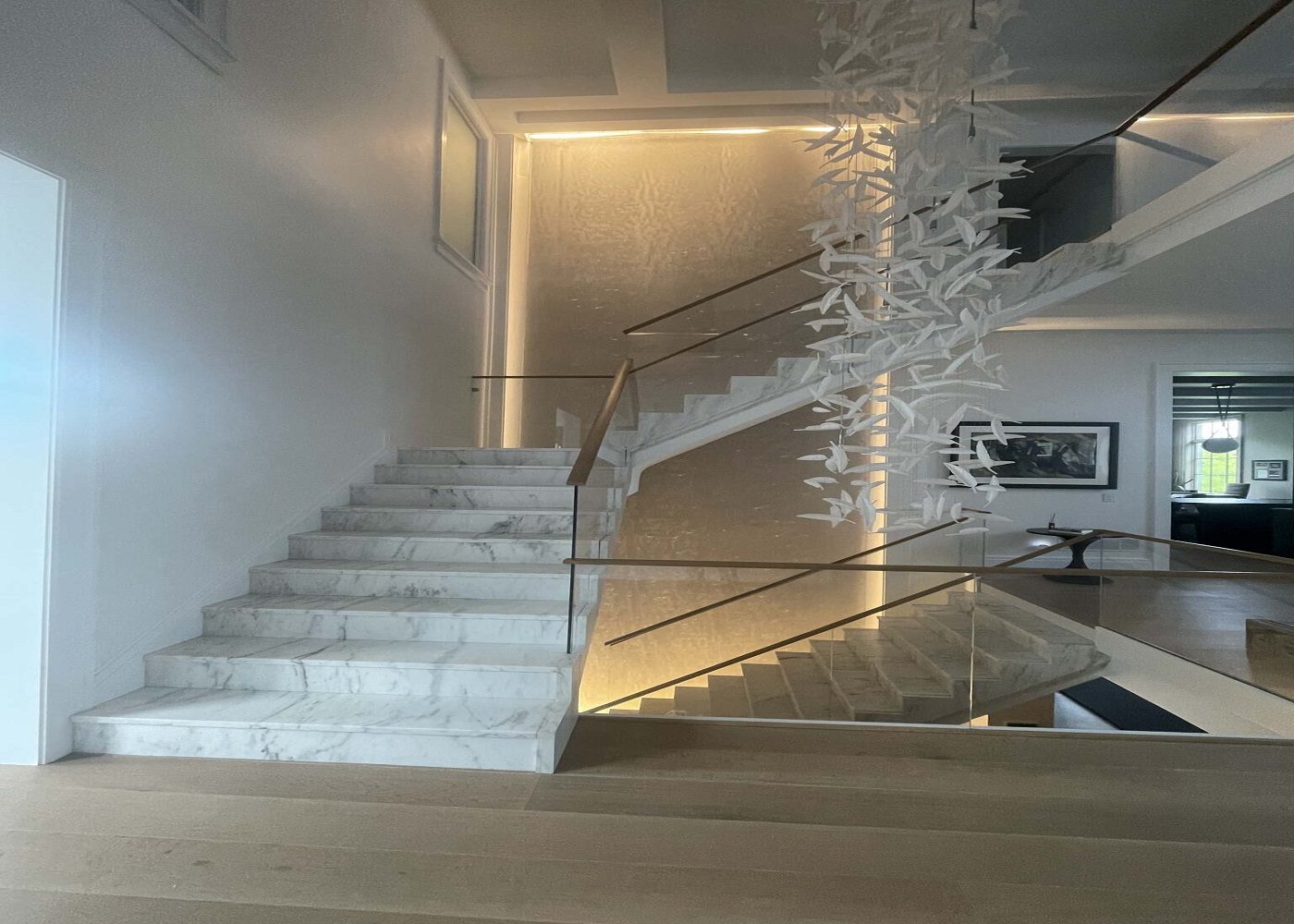 Marble staircase with modern design, illuminated by soft lighting, featuring a decorative wall element of white paper-like shapes, enhancing the aesthetic appeal of the interior space.