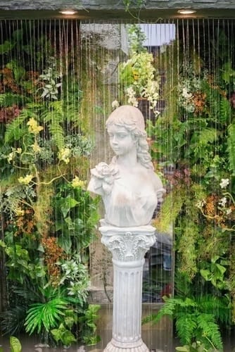 Indoor water feature with a marble bust surrounded by cascading water and lush greenery, enhancing ambiance and tranquility in commercial spaces.