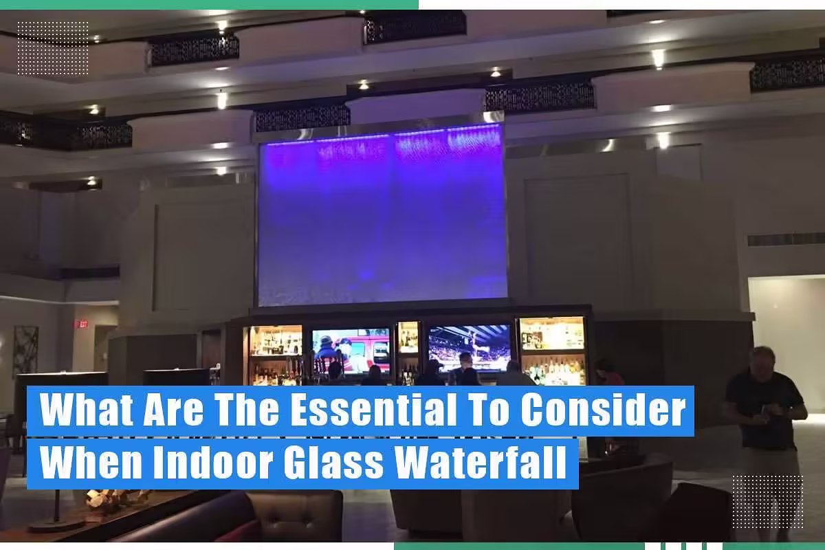 Indoor glass waterfall feature in a commercial setting, illuminated with blue lighting, enhancing aesthetic appeal; bar area visible in foreground.