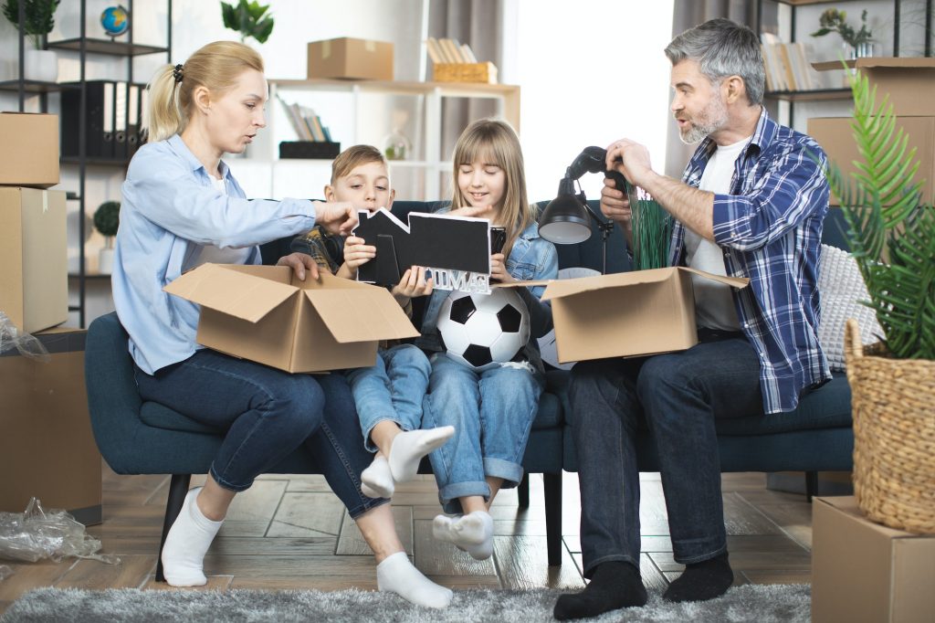 Young parents with kids unpacking boxes during relocation to new appartment