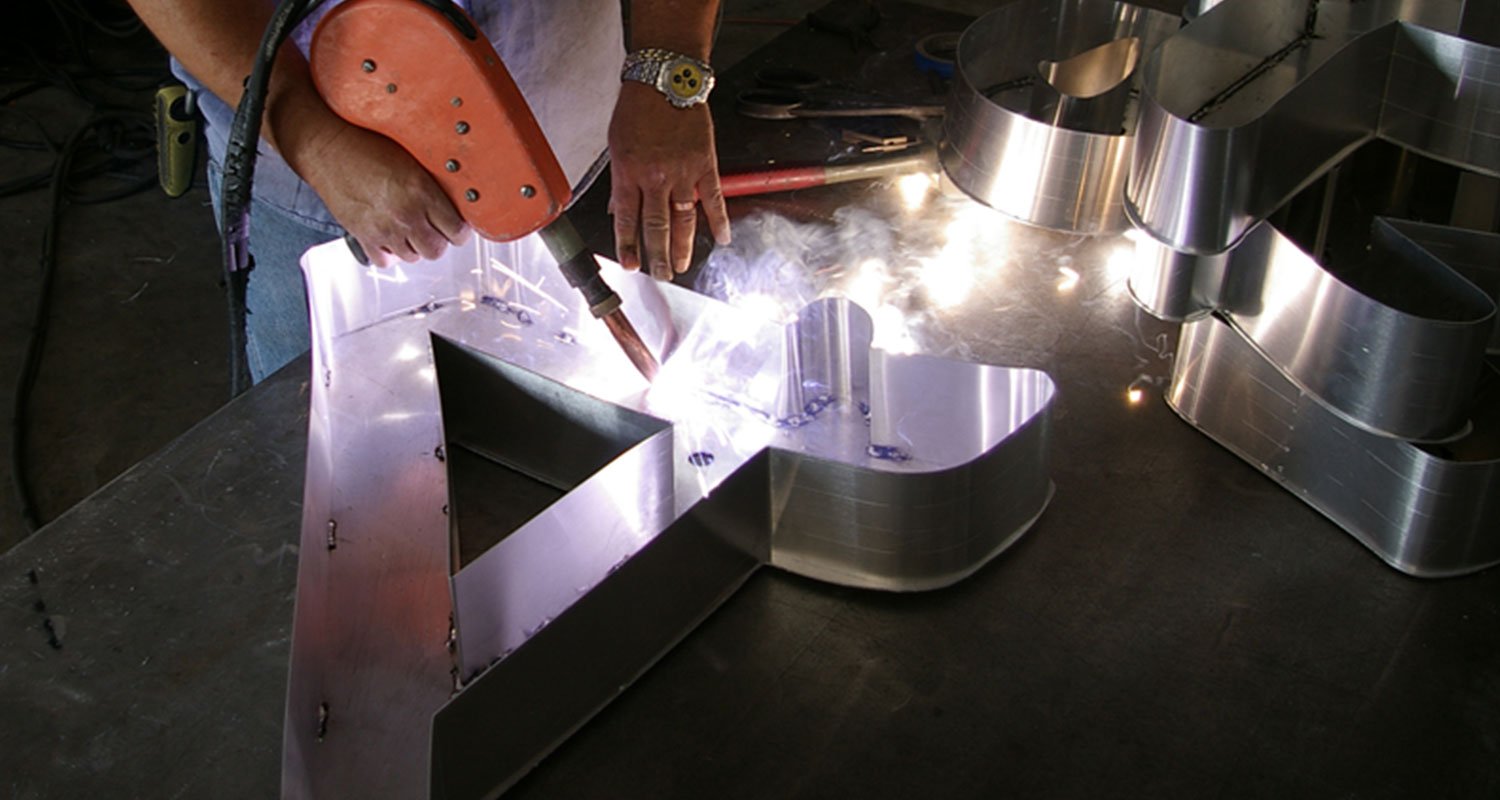 what-is-a-signage-company - City Signs of Texas Craftsman welding a metal channel letter sign for commercial use.