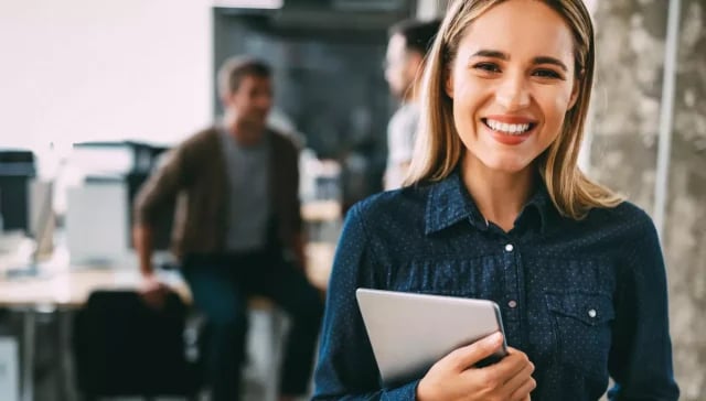 Eine lächelnde Frau mit einem Tablet in der modernen Büroumgebung einer Online-Marketing-Agentur.