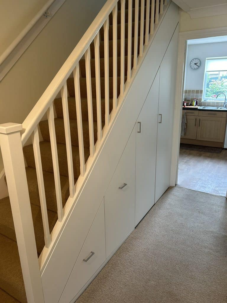 White storage drawers designed for under-stair spaces.