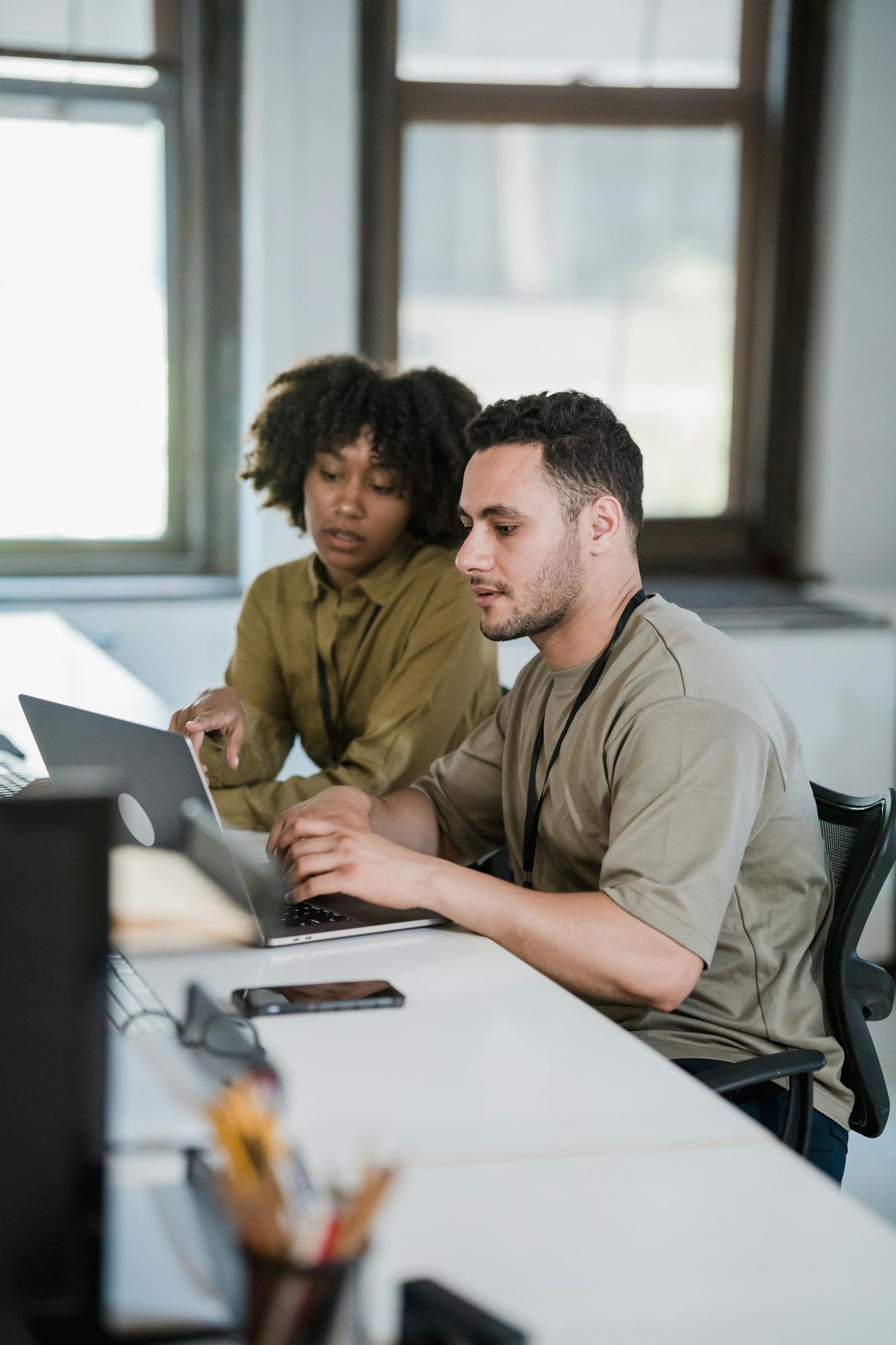 Two colleagues working together on a laptop in a modern office setting.
