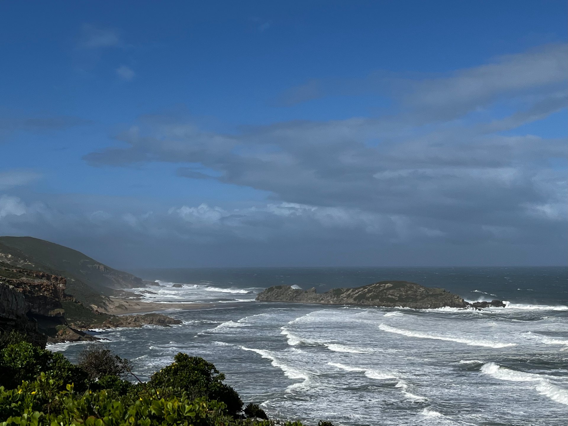 Dark clouds gathering over a see with high waves and part of the coastline in Robberg Nature Reserve. One of our best hikes on the Garden Route