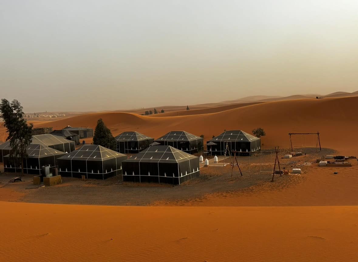 Campsite in the desert with black tents amidst shifting sand dunes and scenic landscape.