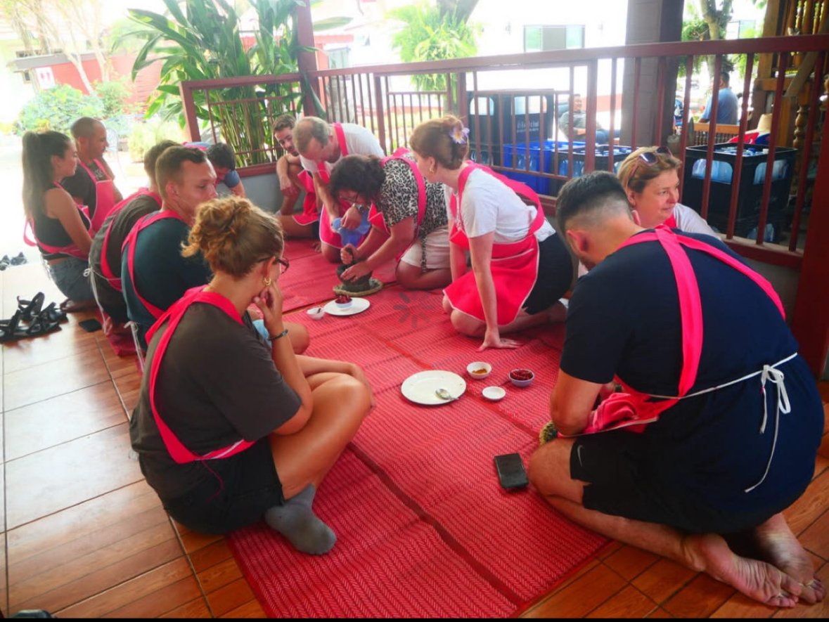 Making curry in Thai cooking class: woman using a amortar and pestle with group looking on.