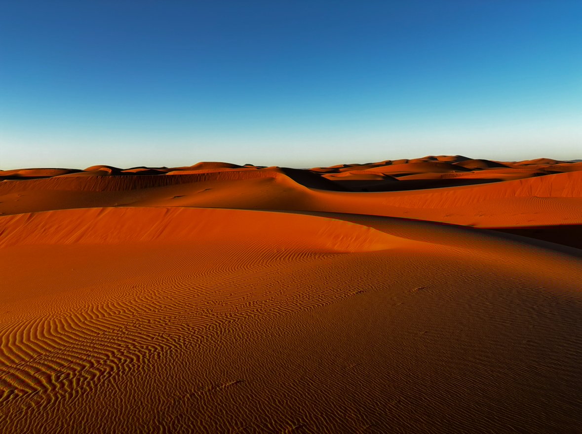 Expansive desert landscape with orange sand dunes and bright blue sky.