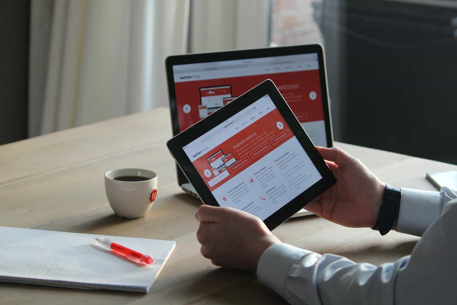 Elementor Page builder, website, development, design, drag n drop, wordpress, Business professional using a tablet and laptop with a hot drink, focusing on digital content review.