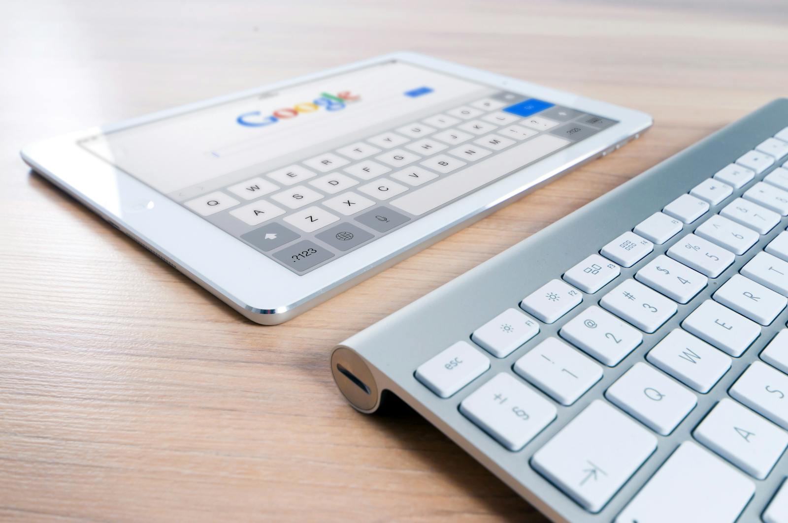 A modern tablet displaying a search engine logo next to a wireless keyboard on a wooden desk. SEO Strategies for Online Success