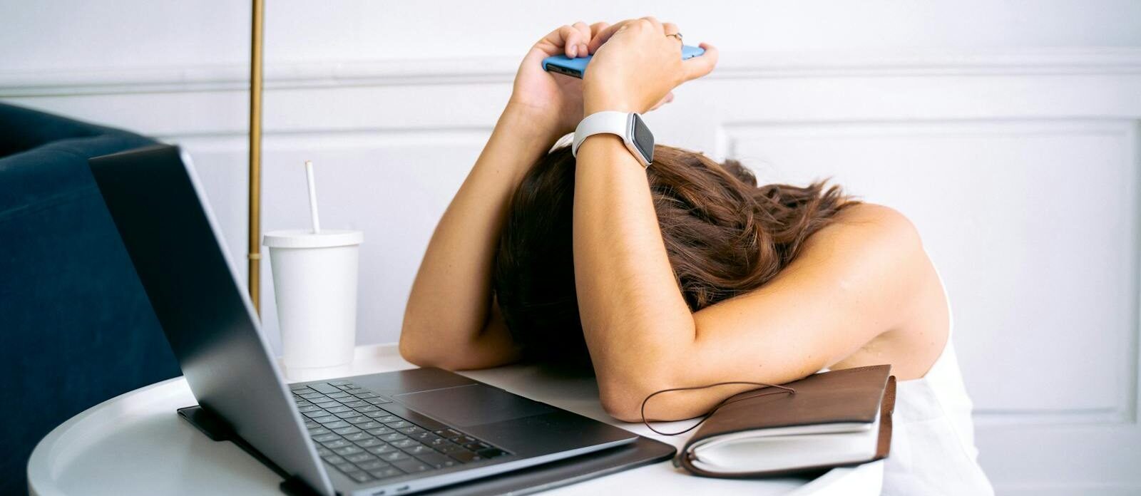 Young woman showing stress with laptop and phone at desk, embodying digital exhaustion.