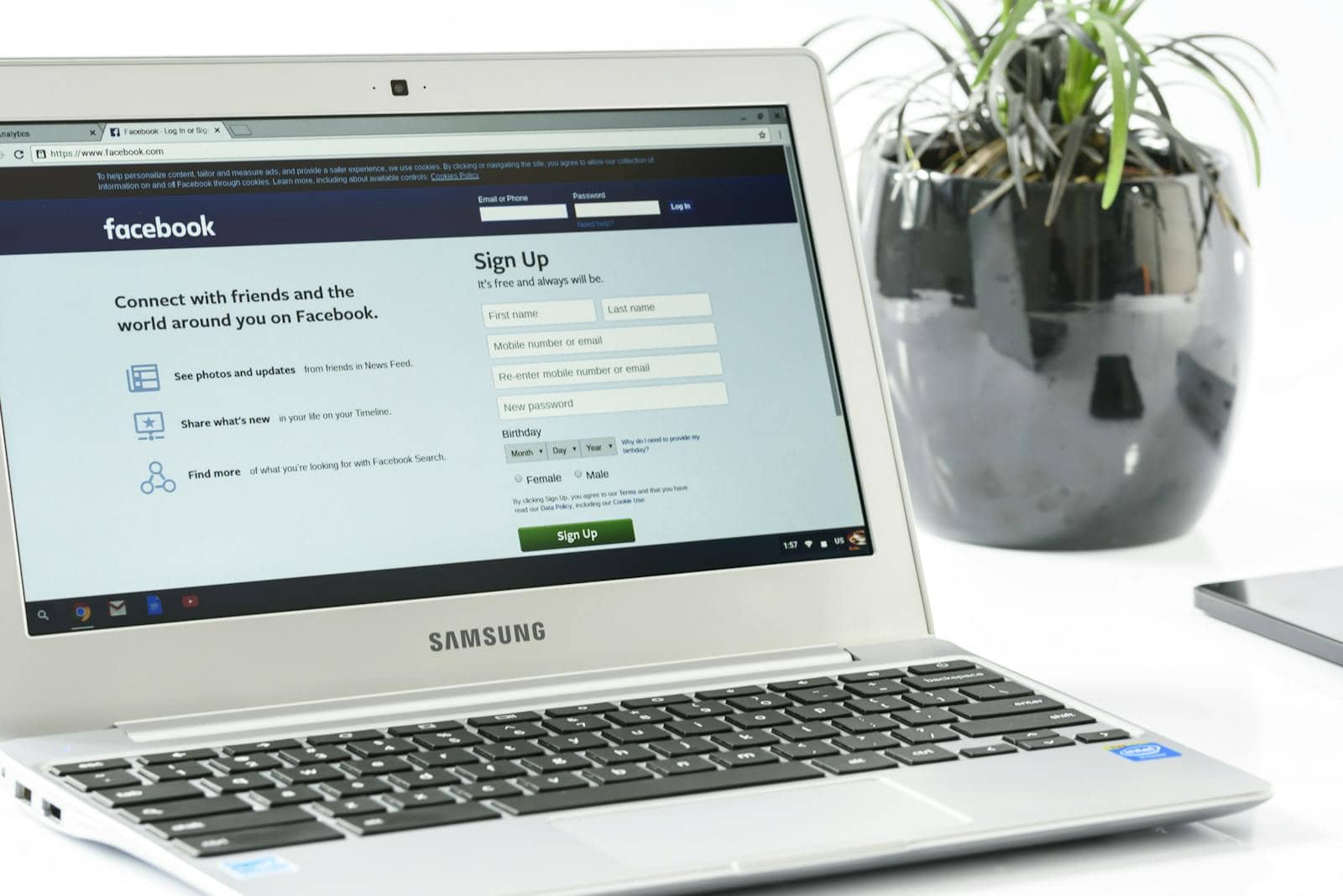 facebook, engagement, live, Open Samsung laptop showing Facebook sign-up page next to a potted plant. Ideal for technology themes.