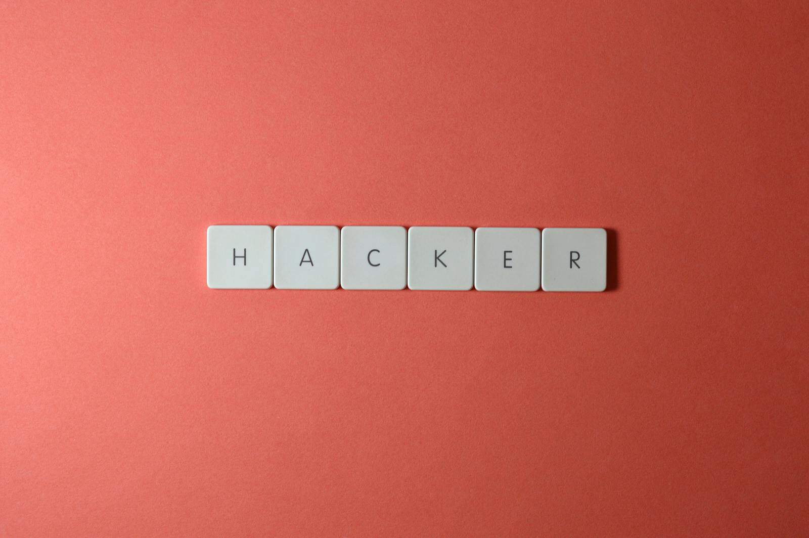 Password Management, Close-up of the word 'HACKER' made with letter tiles on a red background, emphasizing cybersecurity.