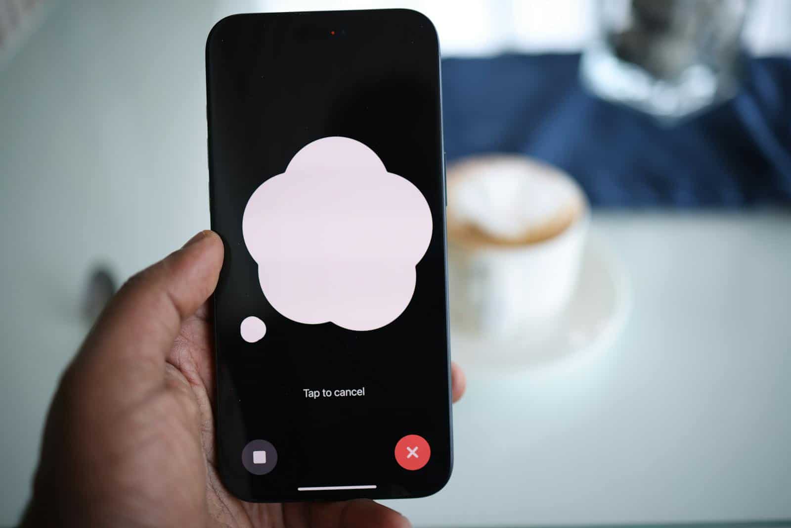 Speech recognition technology, Close-up of a smartphone in hand with AI voice chat bubble and coffee in background.