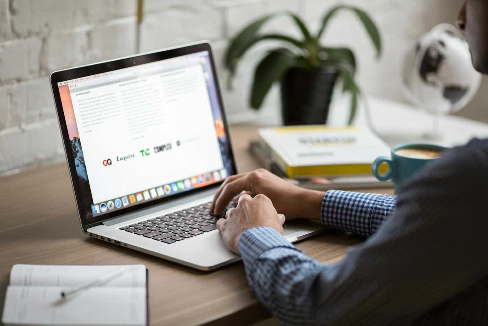 email deliverability, A man working on a laptop at a desk with coffee, showcasing remote work in a modern office setting.