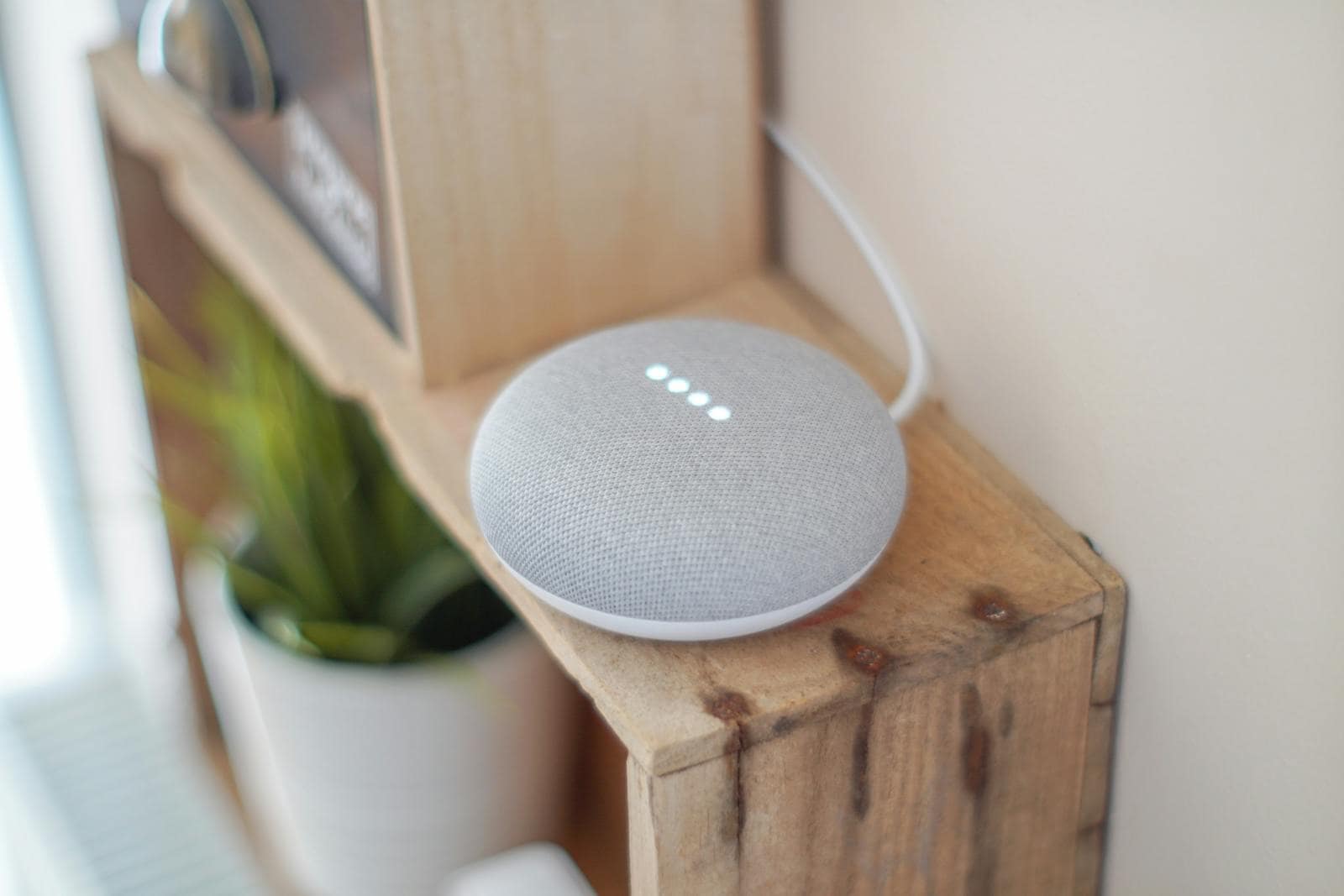 Speech recognition technology, A Google Home Mini smart speaker on a wooden shelf, blending technology with home decor.