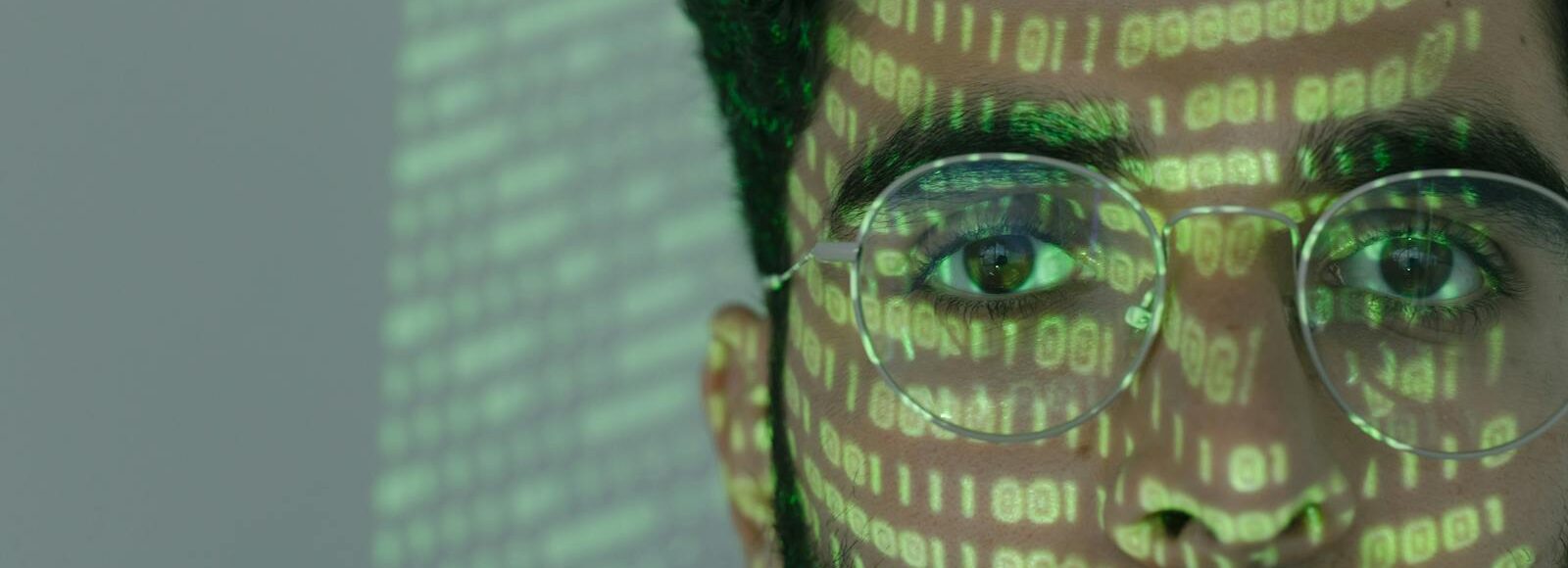 Close-up of a man with binary code projected on his face, symbolizing cybersecurity.