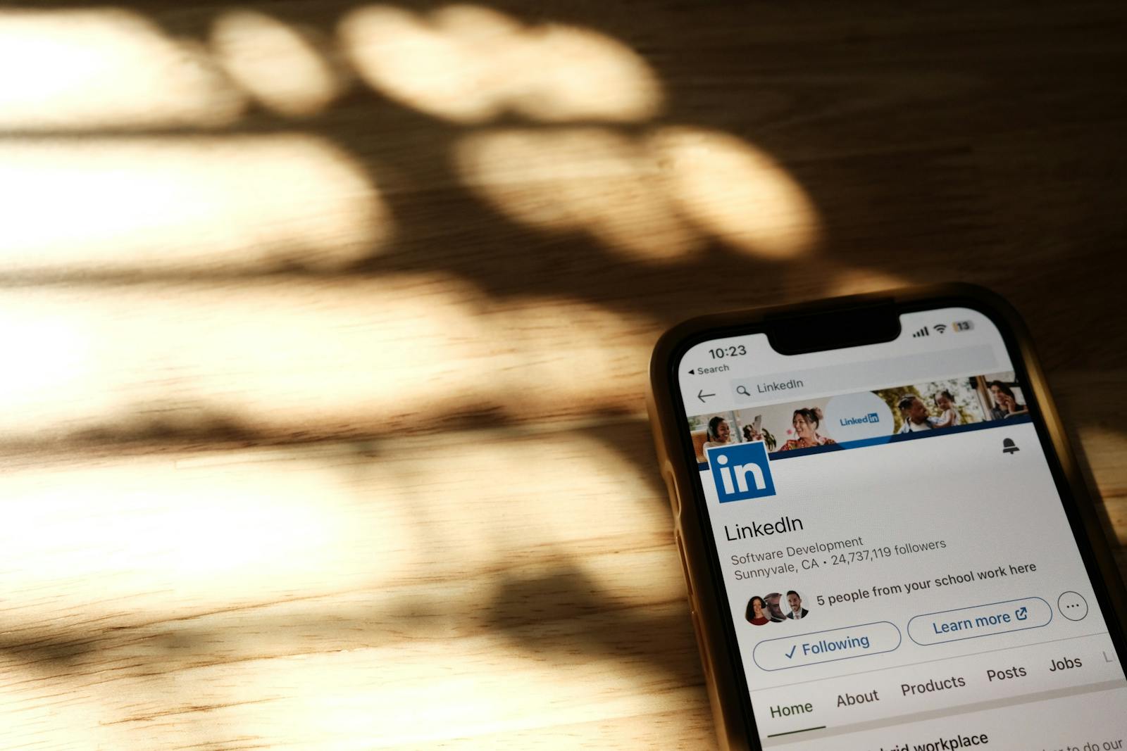 LinkedIn Marketing, Close-up of a smartphone showing a LinkedIn profile page on a wooden table with shadows.