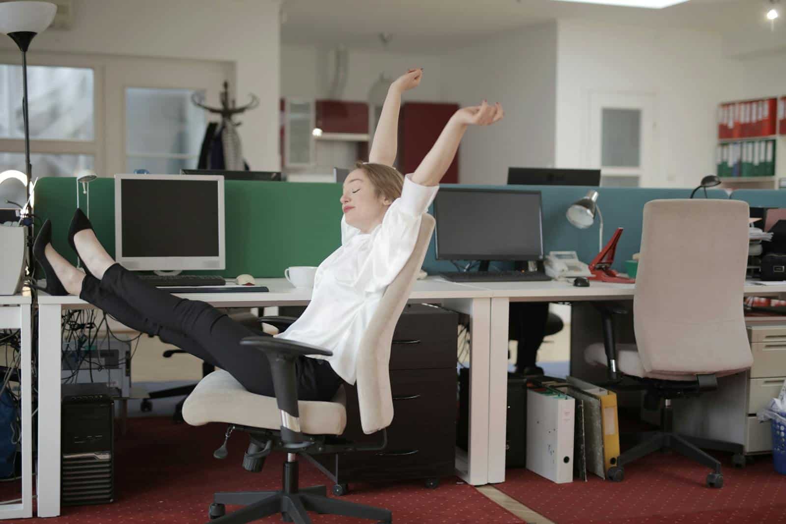 Effective Time Management Tips: Boosting your Productivity, Side view of cheerful female employee in formal outfit sitting on office chair with crossed legs on desk and stretching while resting during work with closed eyes