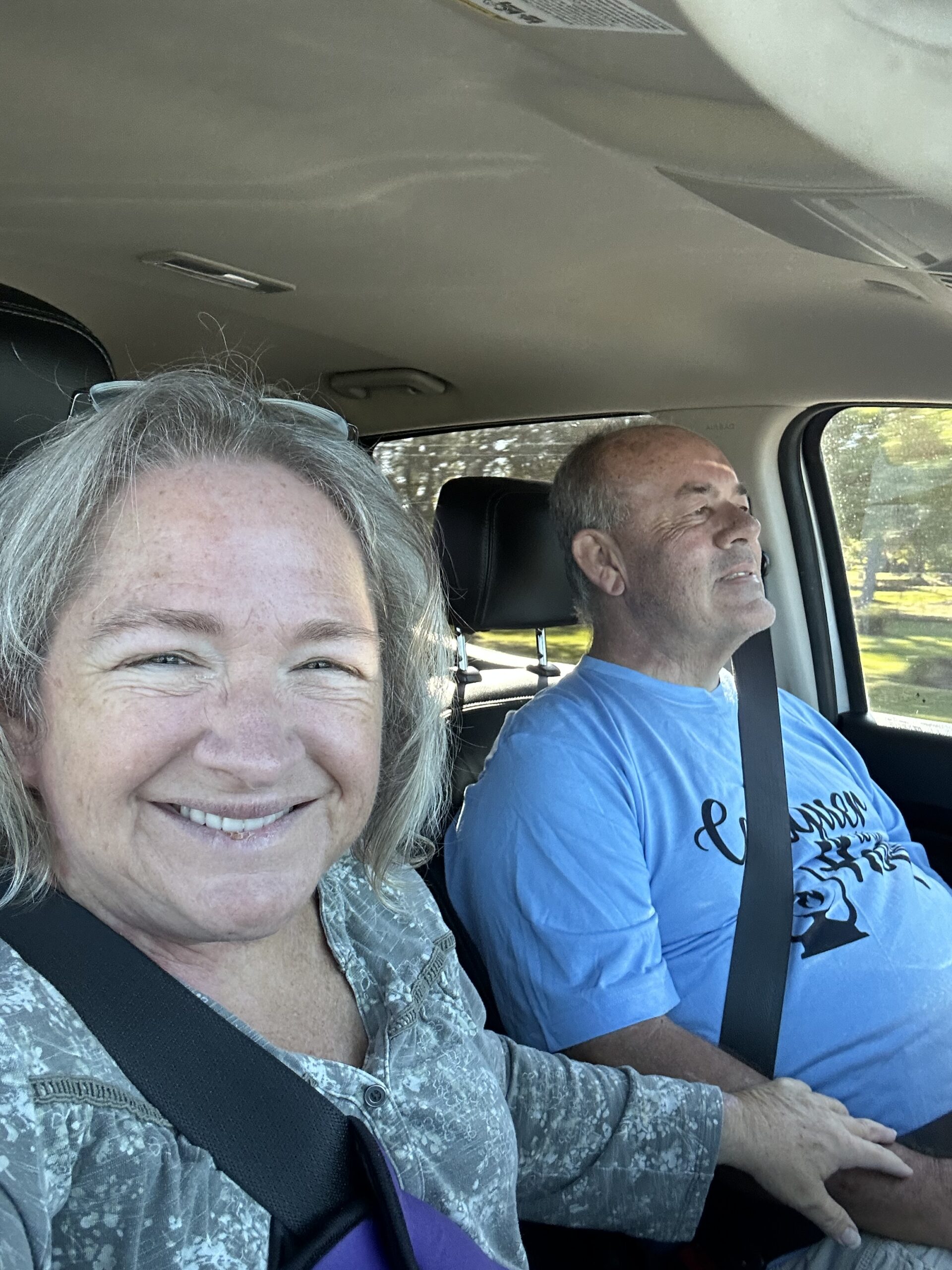 Amy & Ken in the truck, seat belts on and smiling as they travel.