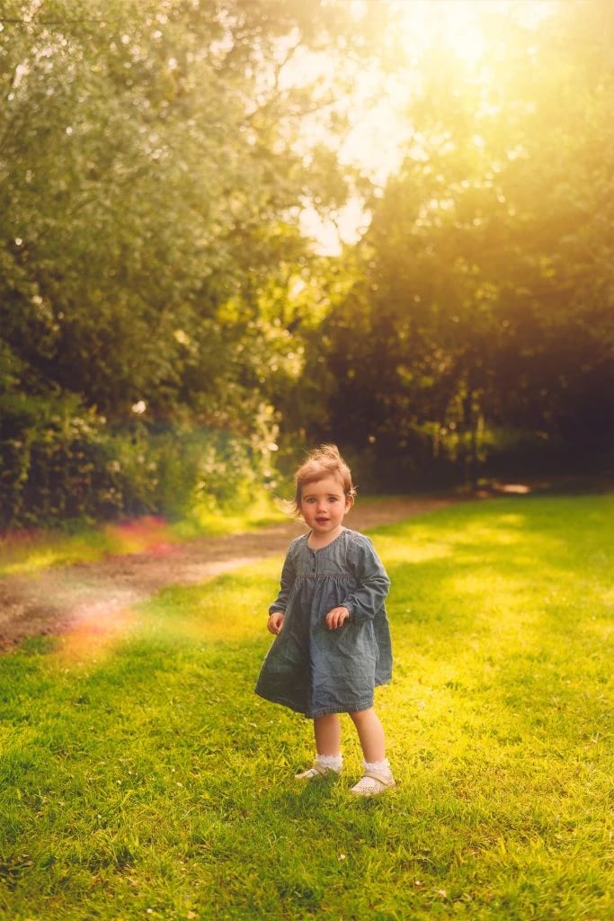 Family Photographer A little girl standing in a grassy field under the sun captured by a family portrait photographer.
