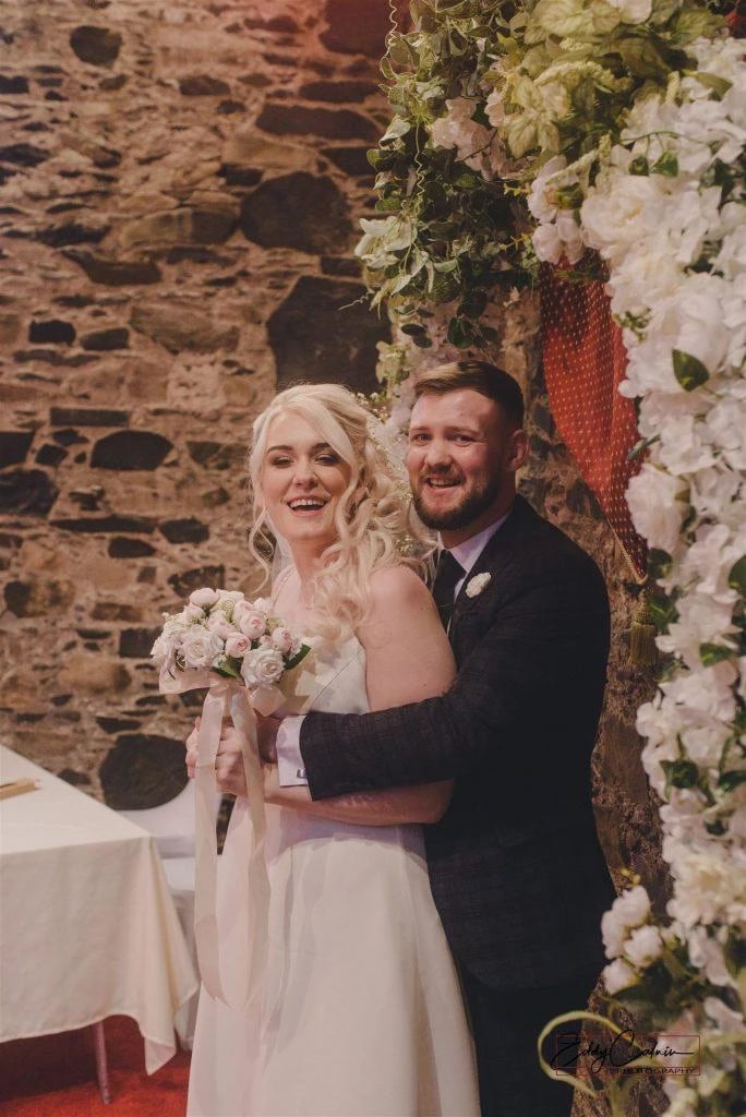 Terri-Leigh & James Corrigan 2 Family Photographer A bride and groom posing in front of a stone wall.