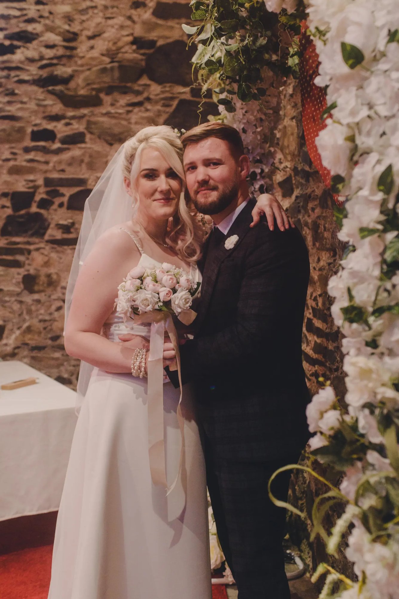 Family Photographer A bride and groom posing in front of a stone wall captured beautifully by a wedding photographer.