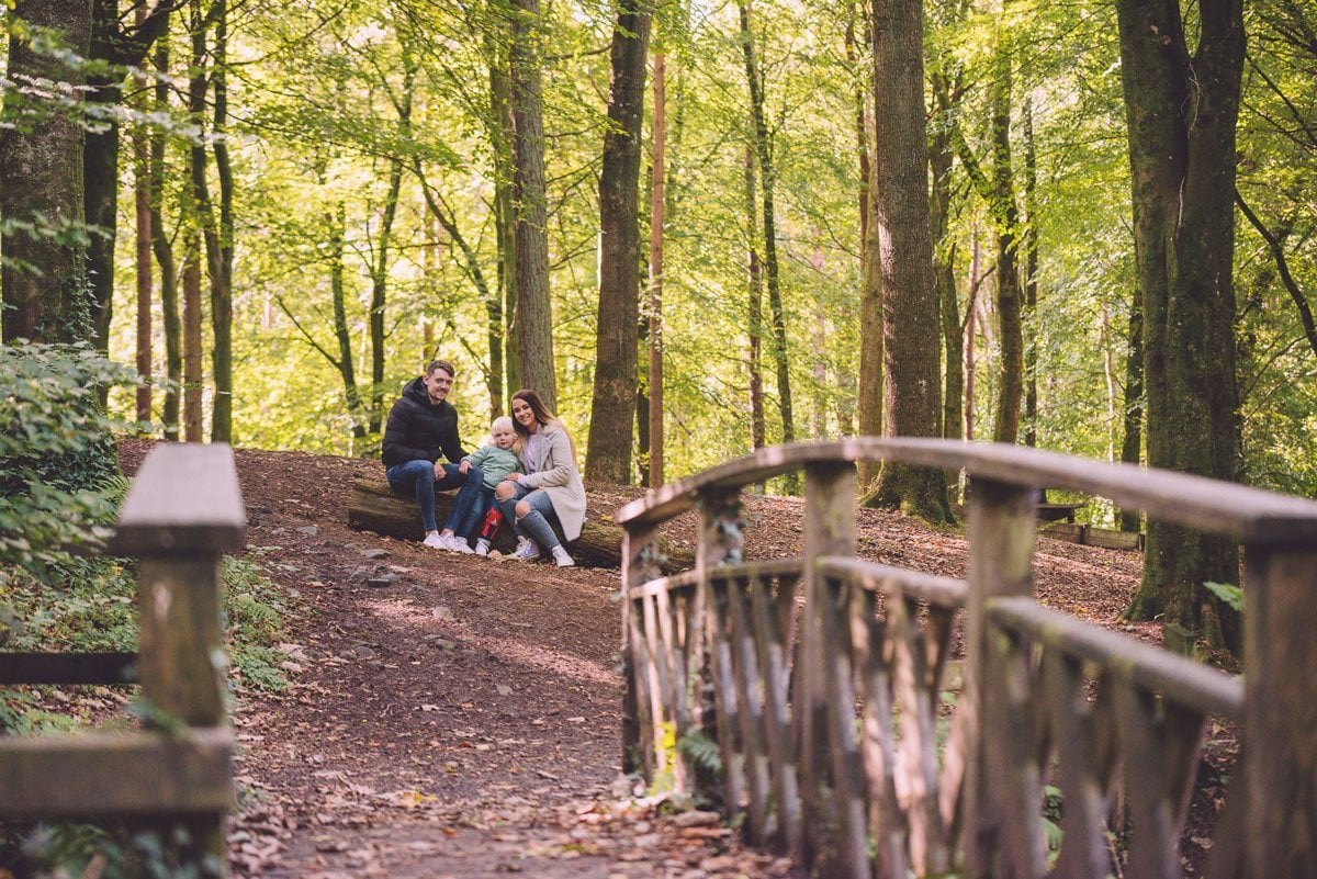 Professional Family Photographer in Ballymena, Northern Ireland 1 A group of people sitting on a wooden bridge in a wooded area.