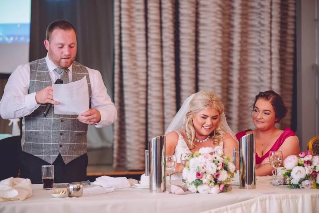 The Best Wedding venues - The Royal Court Hotel Portrush 4 Family Photographer A man is reading a speech at a wedding reception.