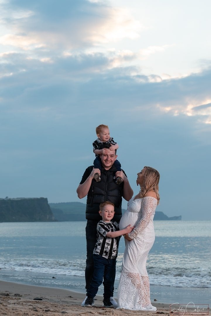 BALLYCASTLE MATERNITY PORTRAITS 1 A family is captured by a photographer on the beach in Northern Ireland at sunset.