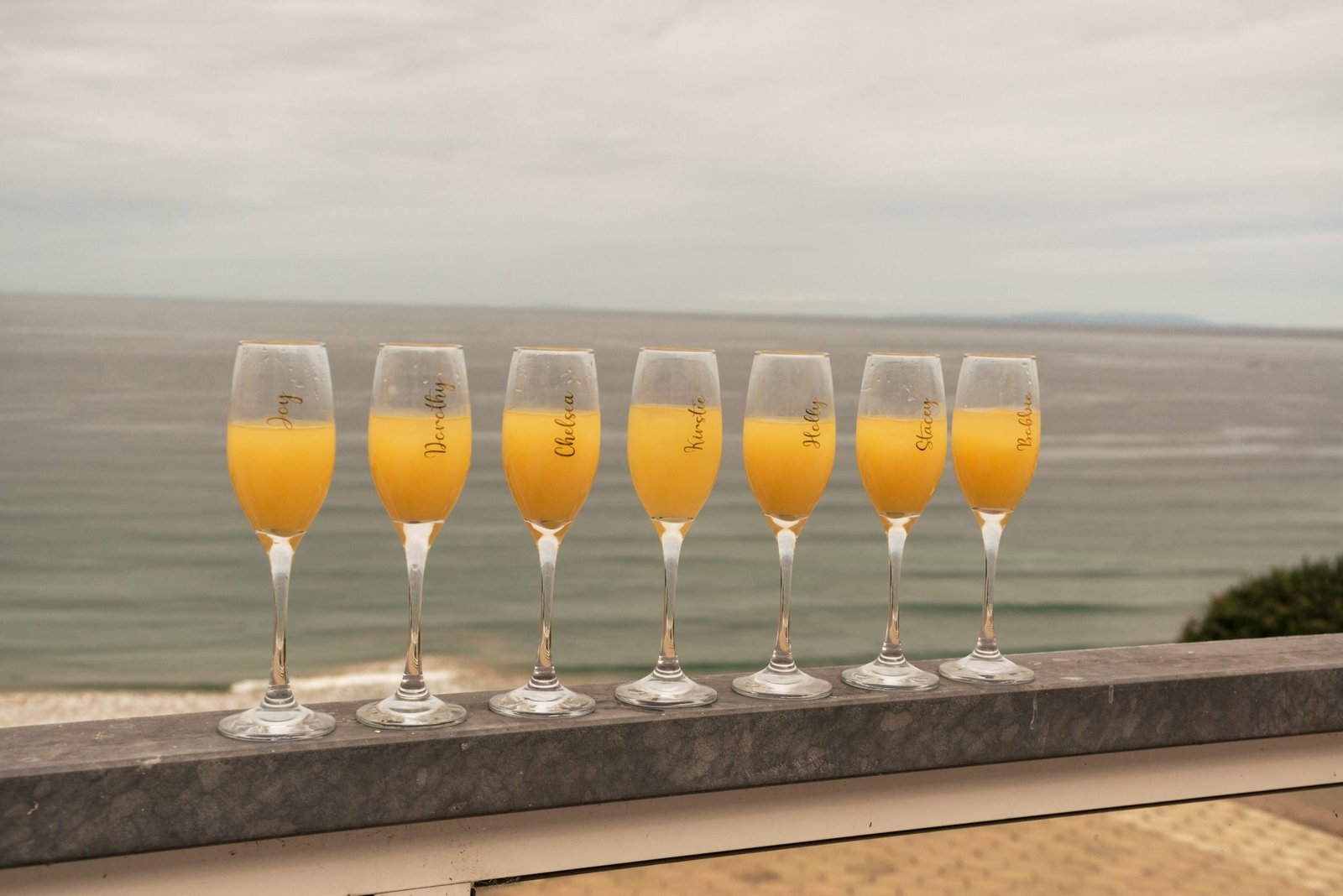 Small Wedding Ideas 3 Family Photographer Row of champagne glasses with orange liquid against a seaside backdrop at the Royal Court Hotel.