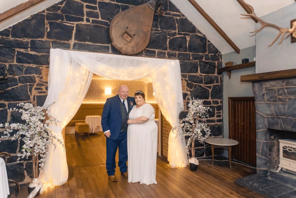 Stranocum Wedding of Sylvia & Alastair 1 Family Photographer A bride and groom standing in front of a stone fireplace.