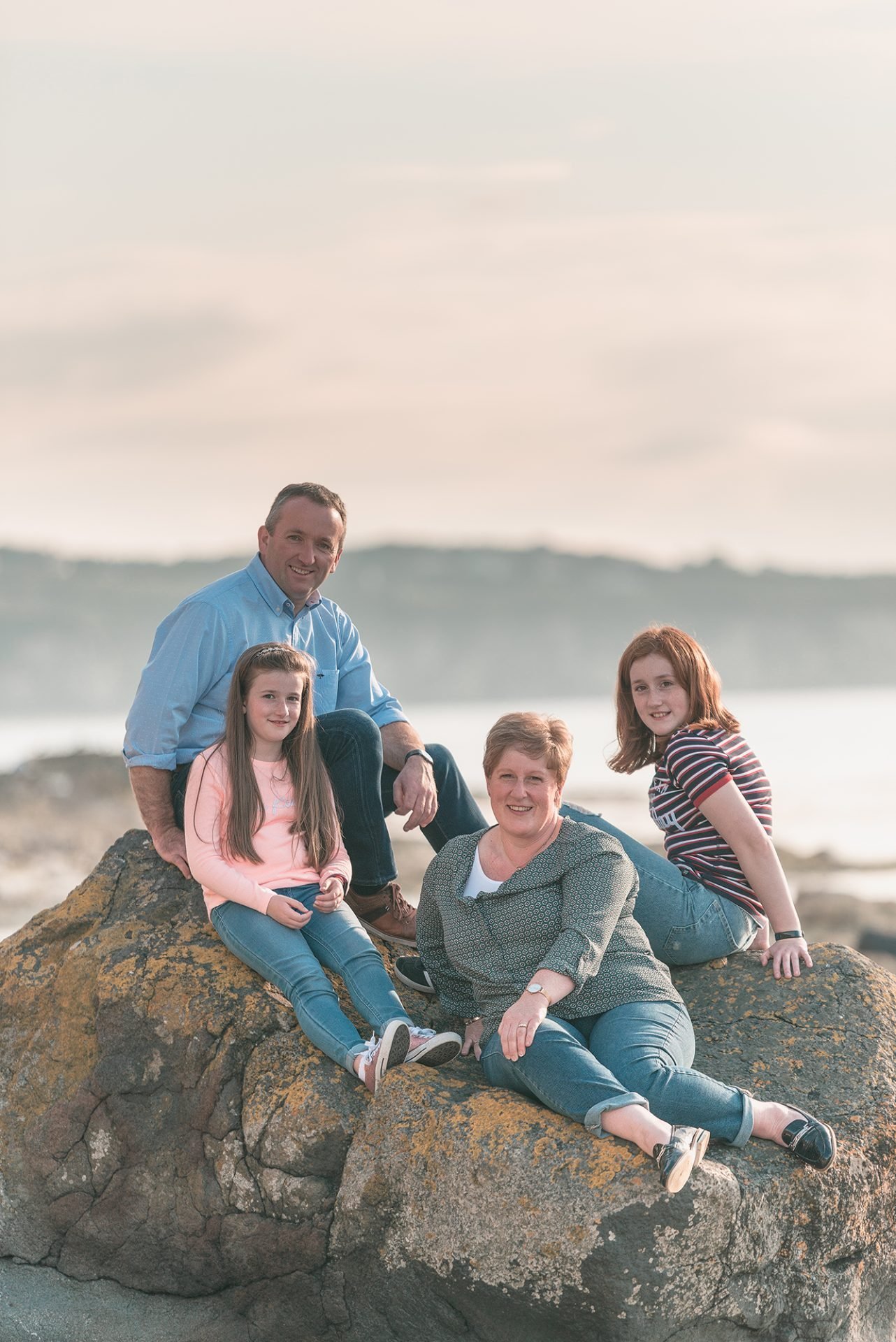 A ni family sits on rocks at the beach.