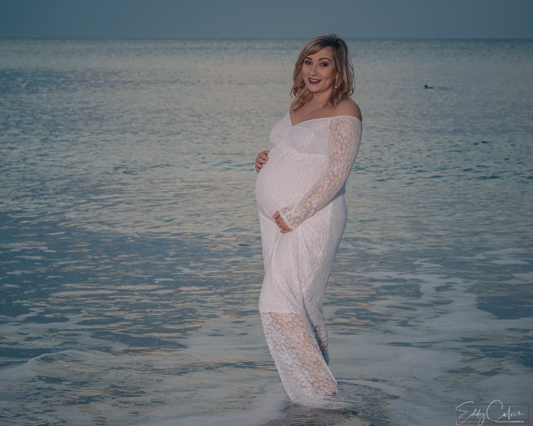 BALLYCASTLE MATERNITY PORTRAITS 3 A pregnant woman in a white dress standing in the ocean, captured by a Northern Ireland family photographer.