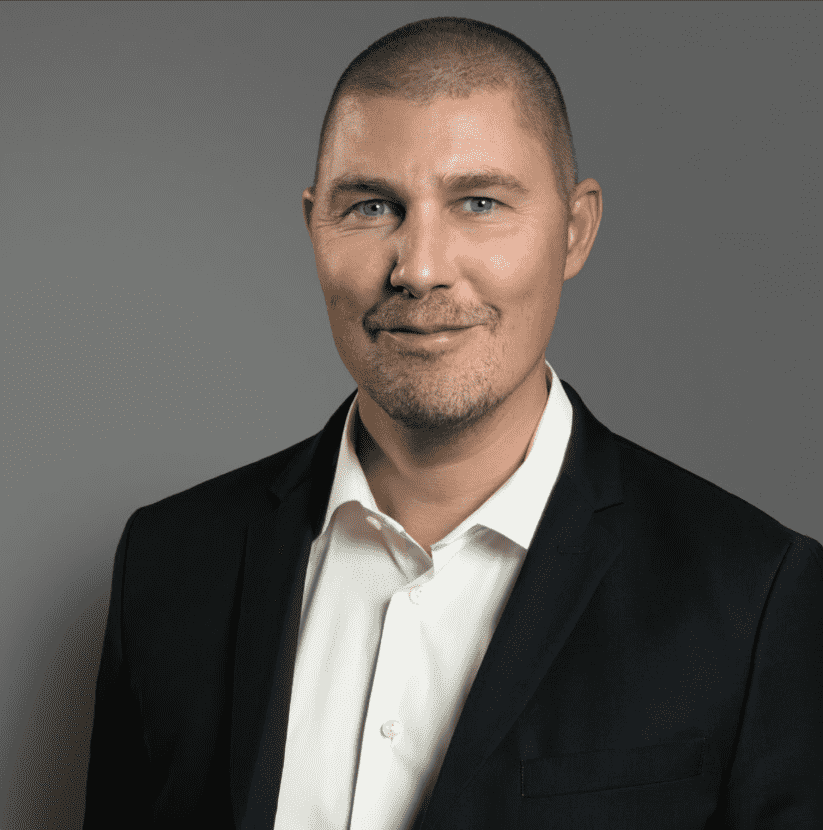 Per bär en vit skjorta och en mörk kavaj och ler lite mot en grå bakgrund. winwinweb